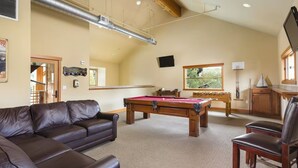 Ein Zimmer mit Poolbillardtisch, Ledersofa und Holzschrank.