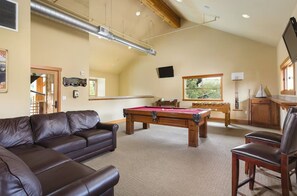 Ein Zimmer mit Poolbillardtisch, Ledersofa und Holzschrank.