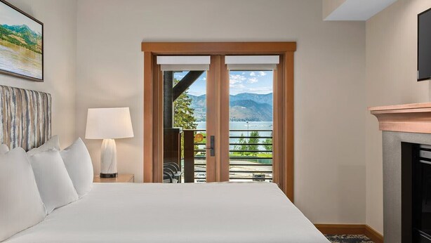 Ein Hotelzimmer mit Bett, Gemälde, Lampe, Kamin und einem Balkon mit Seeblick und Bergblick.