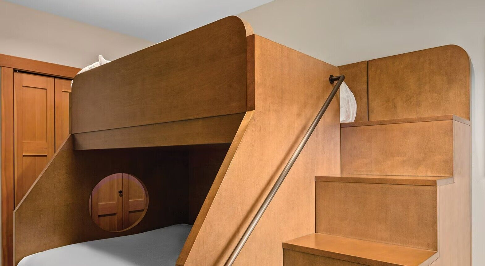 Habitació moderna amb literes, un armari de fusta i una porta rodona.