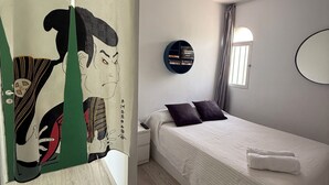 Een slaapkamer met een bed, een nachtkastje, een rond spiegel aan de muur, en een raam met gordijnen.