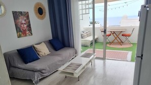 Een moderne woonkamer met een bank, een salontafel en uitzicht op de zee door een glazen deur.