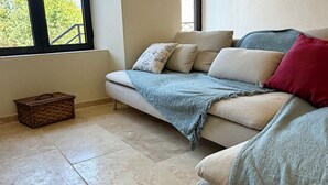 Uma sala de estar com um sofá, uma mesinha e uma janela com vista para árvores.