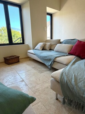 A living room with a sofa, a small table, and a window with a view of trees. - Les Granges du Canal • Charming accommodation with a view and access to the canal (Vions)
