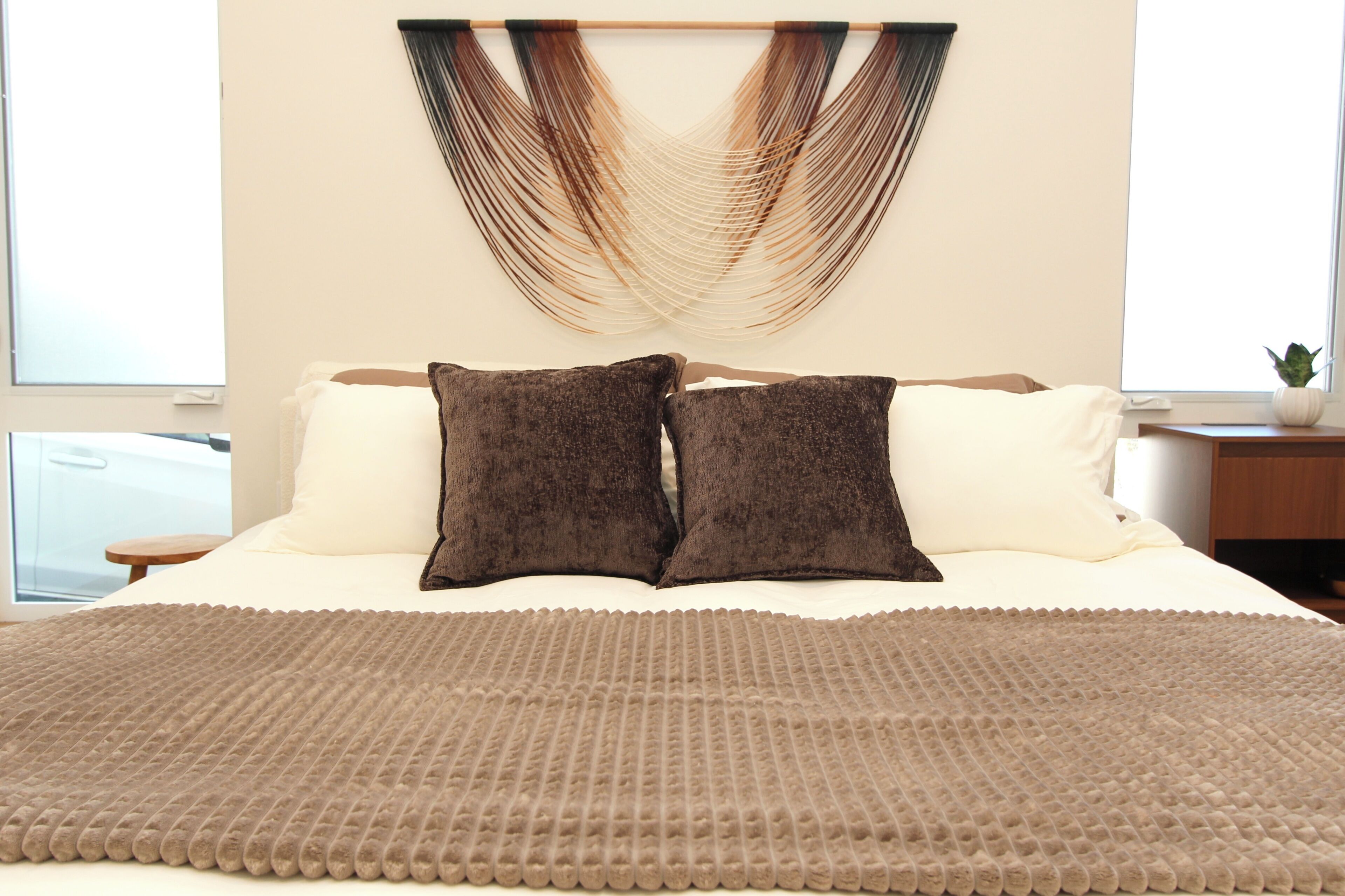 A bed with two pillows, a textured blanket, and a wall hanging.