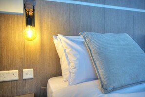 Camera d'albergo con un letto, cuscini bianchi, una lampada a parete e una presa di corrente.