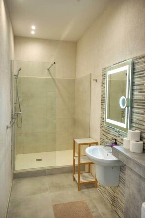 Un bagno moderno con cabina doccia in vetro, ripiano in legno, lavandino e specchio con illuminazione.