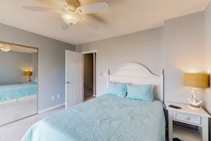 Ein Schlafzimmer mit einem Bett, einem Nachttisch, einer Lampe, einem Deckenventilator und einer Tür zu einem anderen Raum.