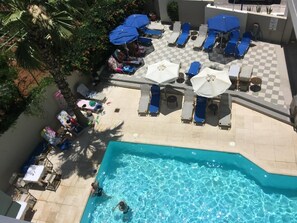 Uma área de piscina no terraço com espreguiçadeiras, guarda-sóis e piso xadrez.