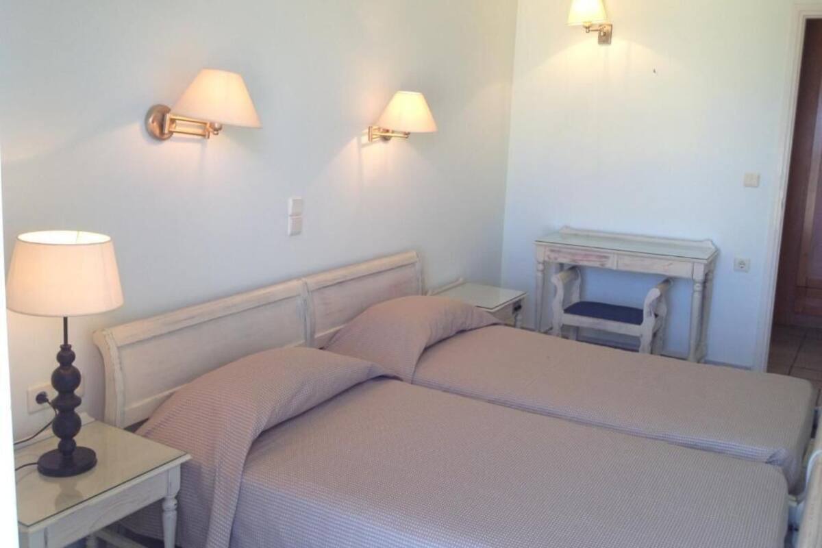 Quarto com duas camas, abajures, mesas de cabeceira e uma pequena mesa com luminária.