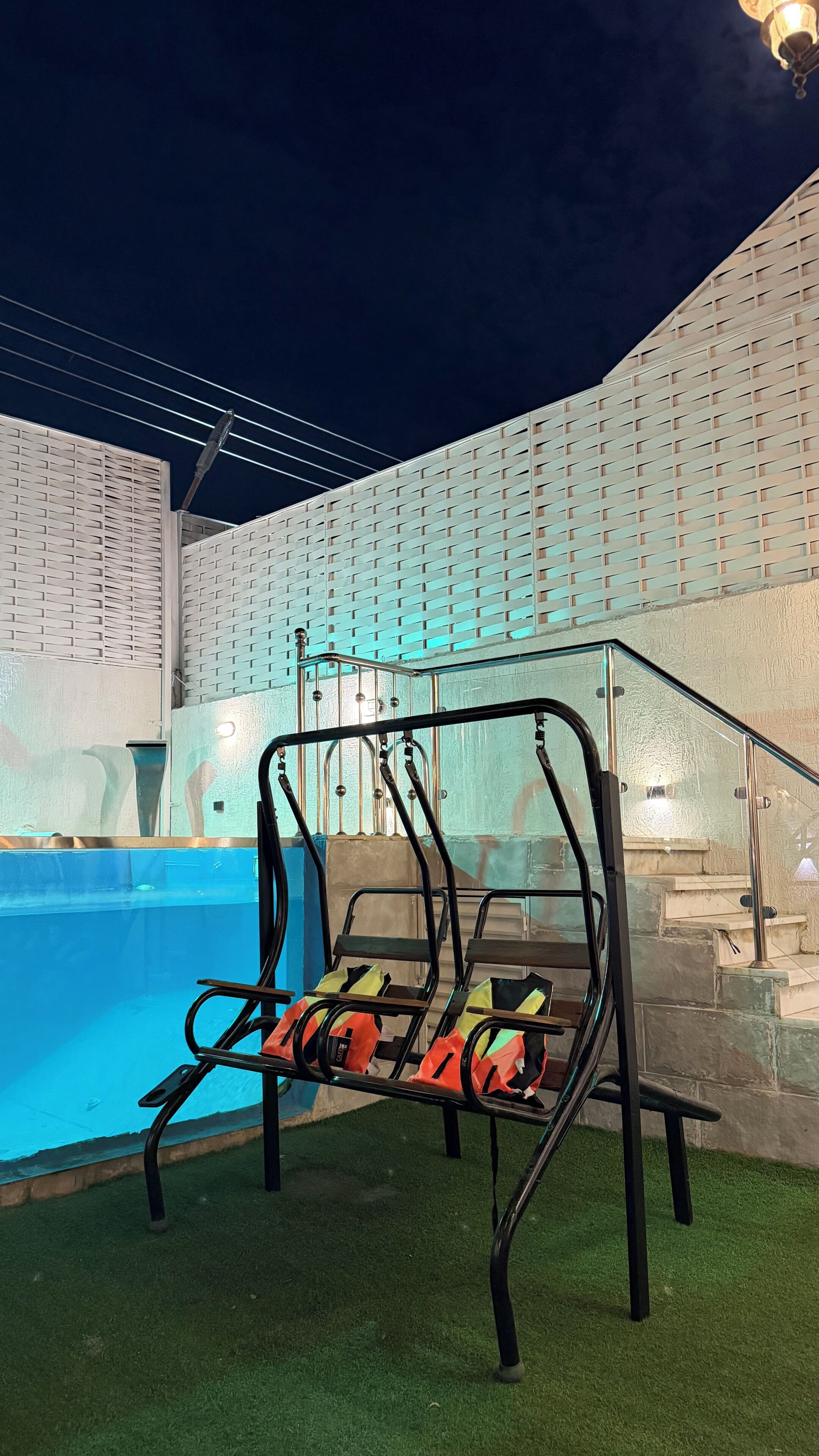 A pool area with a glass railing, a metal structure, and a staircase leading to a higher level.