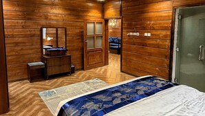 Ein Schlafzimmer mit Holzwandverkleidung, einem Bett mit gemustertem Bettbezug, einem Schminktisch, einem Spiegel und einer Tür zu einem anderen Raum.