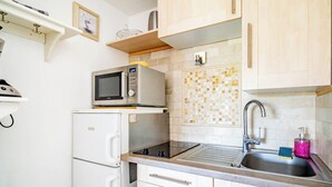 Une cuisine compacte équipée d’un four à micro-ondes, d’un réfrigérateur, d’un évier et de meubles de rangement en bois.