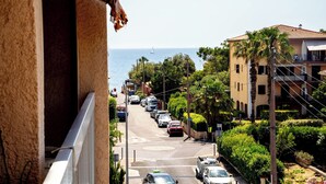 Une rue côtière bordée de voitures garées, un immeuble doté de balcons et une vue dégagée sur la mer.