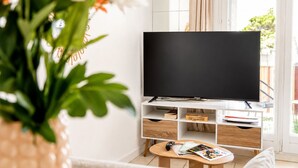 Un salon moderne avec un téléviseur à écran plat posé sur un meuble, une table basse avec des magazines et une plante au premier plan.