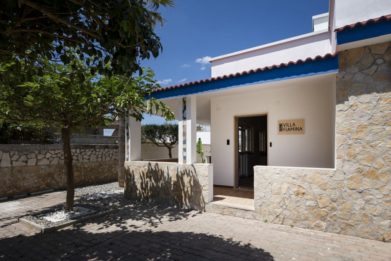 A villa with a stone wall, a blue roof, and a sign reading 'VILLA FIAMINA.'
