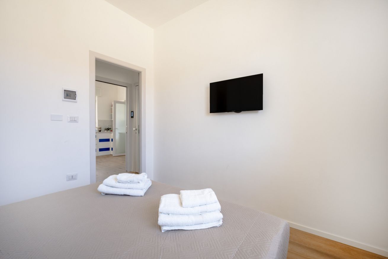 A hotel room with a bed, a flat-screen TV mounted on the wall, and a door leading to a bathroom.