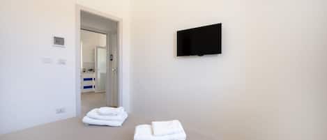 A hotel room with a bed, a flat-screen TV mounted on the wall, and a door leading to a bathroom.