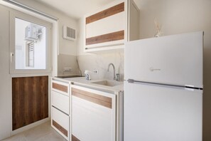A kitchen with a built-in refrigerator, a window with an air conditioning unit, a sink, and wooden paneling on the lower cabinets. - GuestHost - Villa Flamina (Marina di Lizzano)