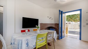 A dining area with a table set for two, a flat-screen TV mounted on the wall, and a brick fireplace. - GuestHost - Villa Flamina (Marina di Lizzano)