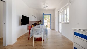 A room with a fireplace, a dining table with chairs, a TV mounted on the wall, and a door leading outside. - GuestHost - Villa Flamina (Marina di Lizzano)