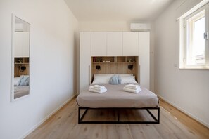 Ein Schlafzimmer mit einem Bett, einem Kleiderschrank, einem Spiegel und einem Fenster.
