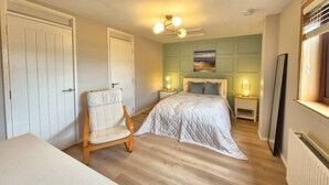 Een slaapkamer met een bed, een stoel, een nachtkastje met een lamp, een plafondventilator en een raam.