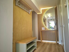 Un pasillo con listones de madera verticales, un banco y una pequeña mesa con un cartel.