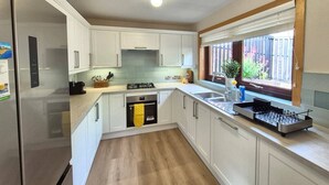 Een moderne keuken met witte kasten, een roestvrijstalen koelkast, een gasfornuis en een raam met uitzicht op groen.