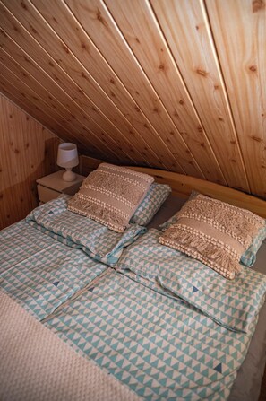 A cozy attic bedroom with wooden slats on the ceiling, a bed with patterned bedding, and a bedside table with a lamp.