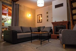 A living room with a sofa, armchair, fireplace, and a table with a plant.