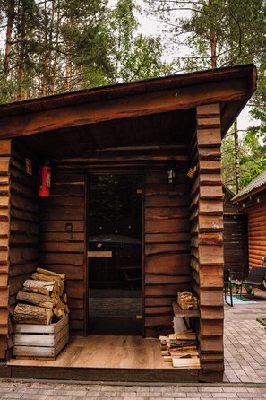 A rustic wooden cabin with a door, a fire extinguisher, and a stack of firewood outside.