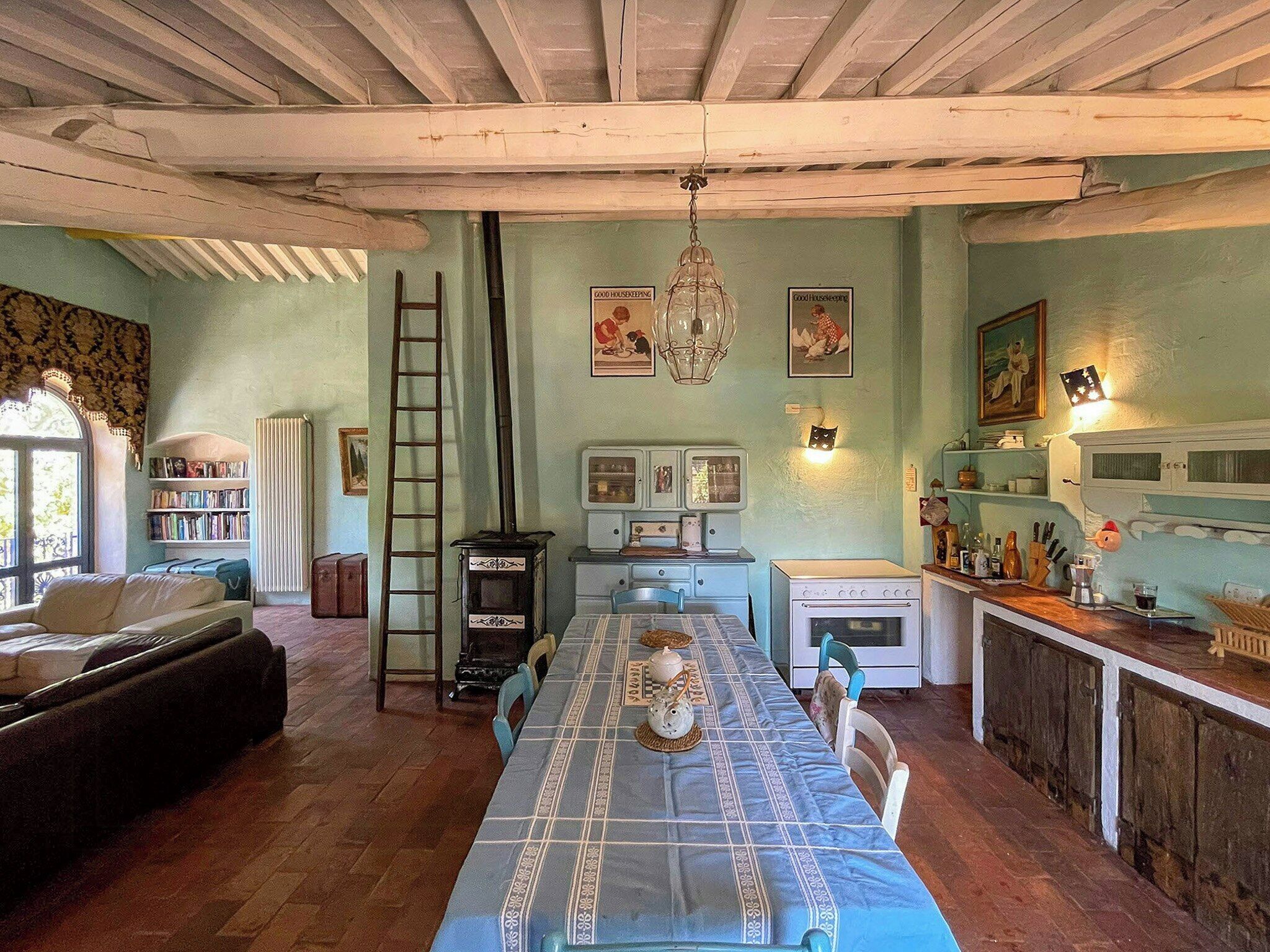 A dining area with a table set for four, a stove, a refrigerator, and a bookshelf.