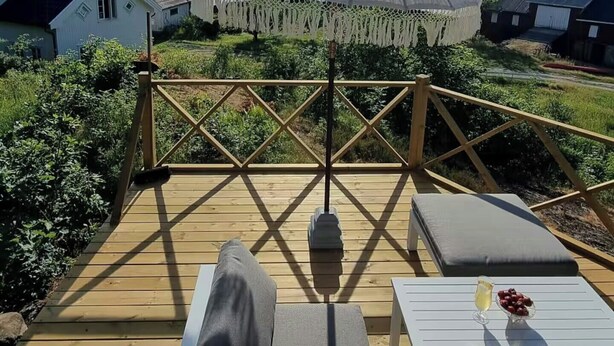 Un terrazzo in legno con un ombrellone grande, poltrone da relax e un tavolo con bevande e frutta.