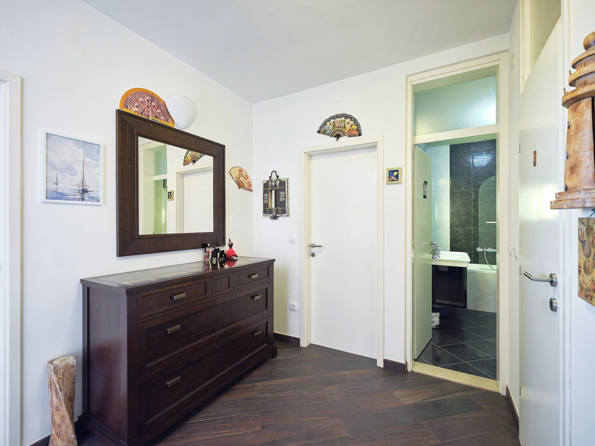 Un couloir avec une commode en bois foncé, un grand miroir et une porte donnant sur une salle de bain.