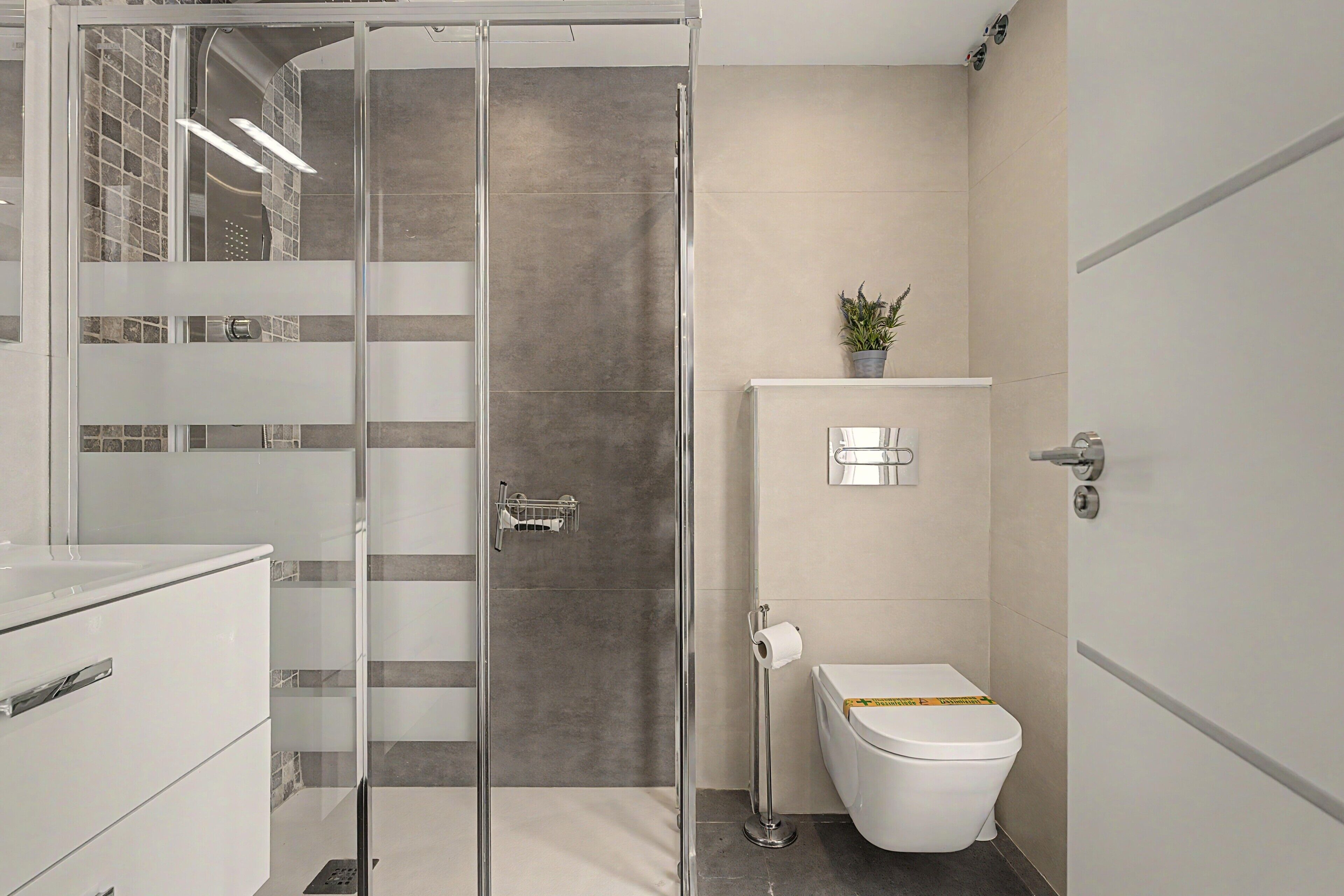 A modern bathroom with a glass shower enclosure, a toilet, and a sink area.