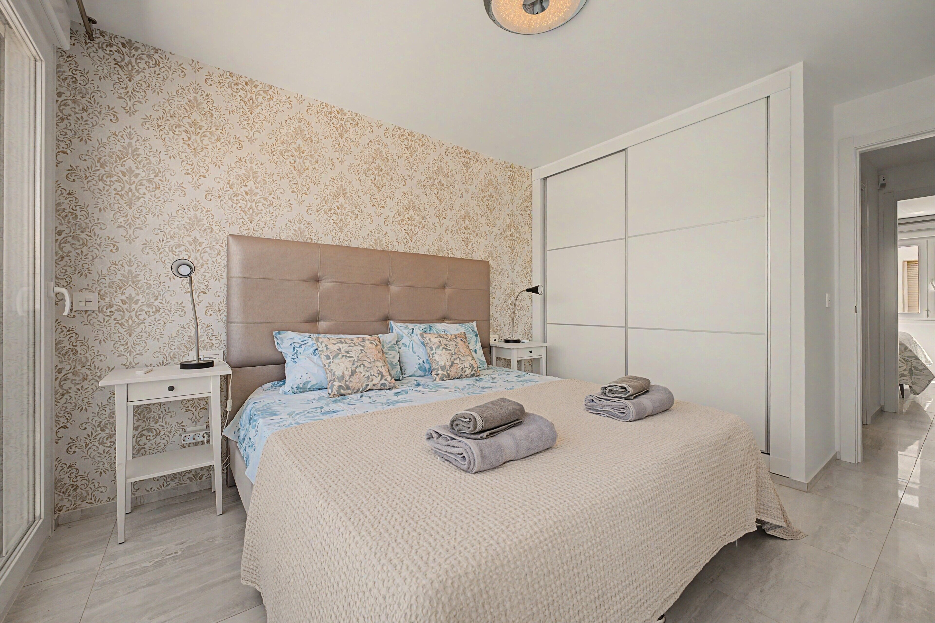 Une chambre avec un grand lit, deux tables de chevet, une armoire et un papier peint à motifs.