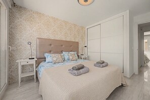 Une chambre avec un grand lit, deux tables de chevet, une armoire et un papier peint à motifs.