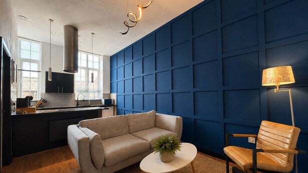A modern kitchen with a blue accent wall, a beige sofa, a small round table with a plant, and a floor lamp. - Urban Lux Apartment | Heart of Town (Warrington)