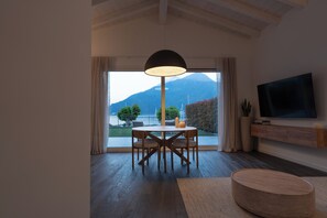Ein modernes Wohnzimmer mit Esstisch, Stühlen, einem runden Couchtisch, einem Fernseher und Blick auf einen Berg.