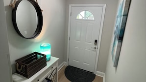 A hallway with a white door, a round mirror, a small table with a candle, and a black rug. - Spacious 3-bedroom townhome, 3 minute walk to the beach, pet-friendly (Myrtle Beach)