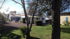 A residential property with a paved driveway, a small lawn, and a house with a tiled roof and blue shutters.