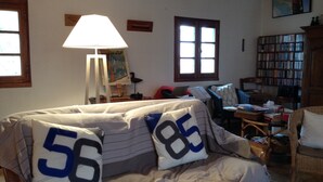A cozy living room with a sofa, a lamp, a painting, a bookshelf, and a window.