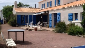 A building with a tiled roof, blue shutters, and outdoor seating with tables and chairs.