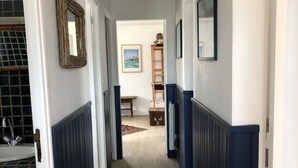 A hallway with dark blue wainscoting, a mirror, a framed picture, and a ladder leading to a room.