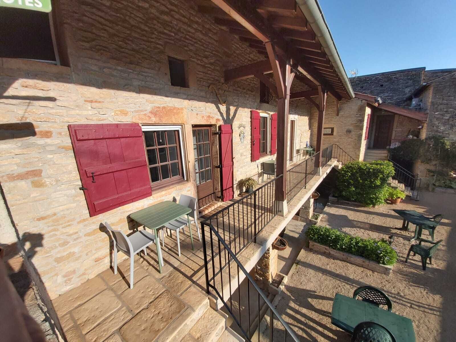 A stone building with a balcony, red shutters, and outdoor seating.