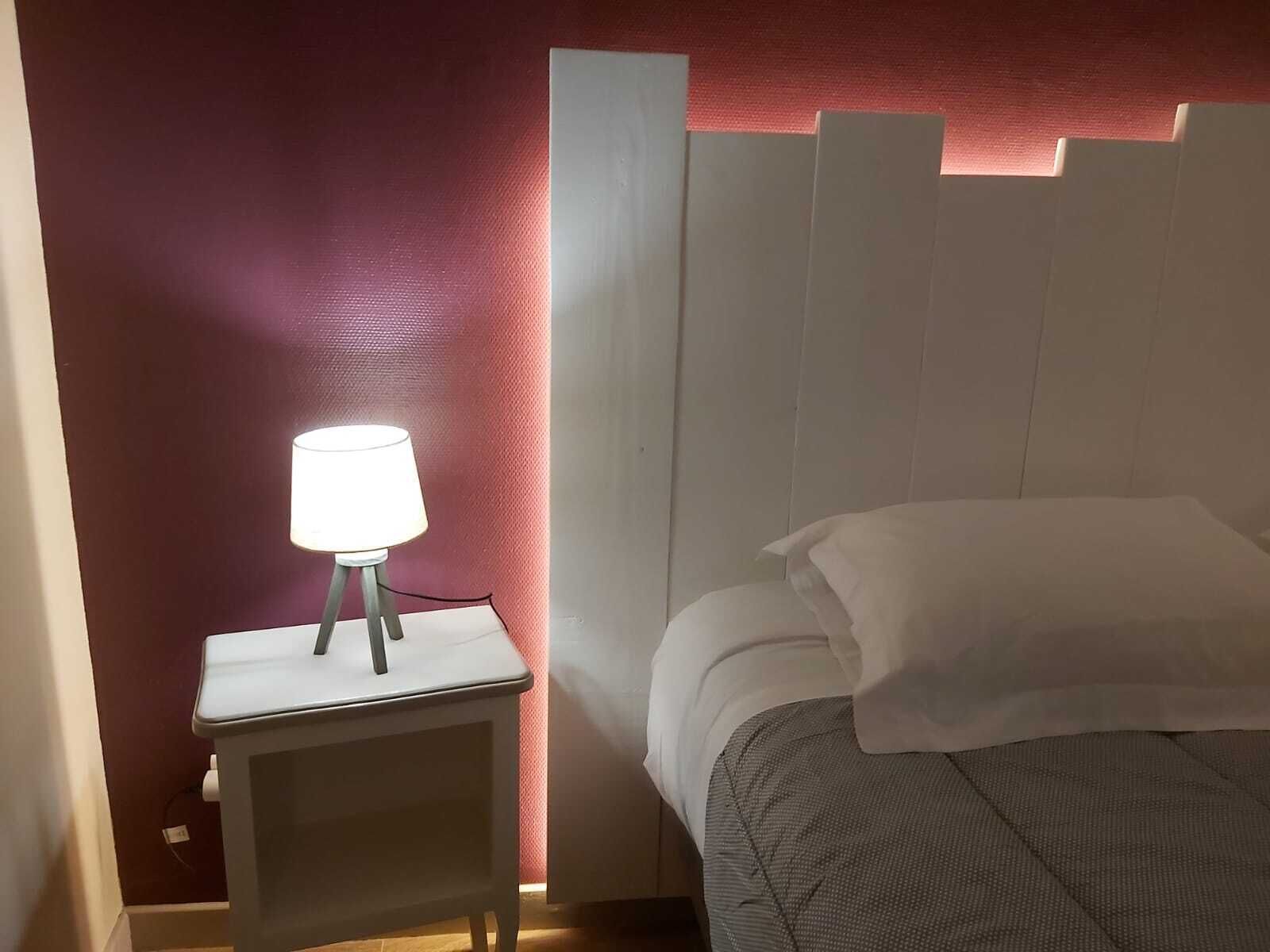 Una cama con ropa blanca, una mesita de noche con lámpara y una pared con diseño de paneles verticales.