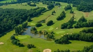 Vista aérea de un campo de golf con múltiples zonas verdes, obstáculos acuáticos y áreas boscosas.