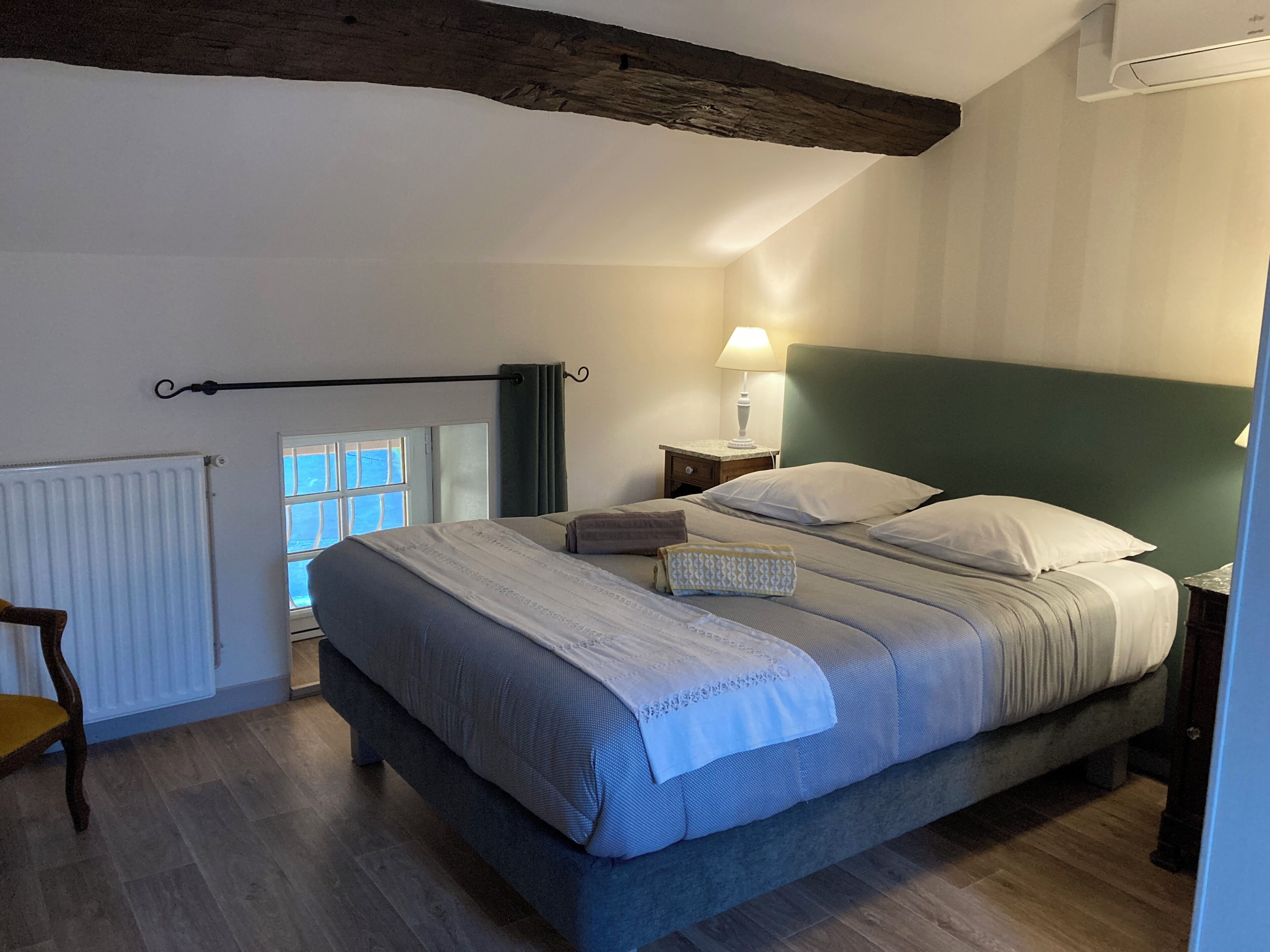 Une chambre à coucher comprenant un lit, une table de chevet, une lampe, une fenêtre et un radiateur.