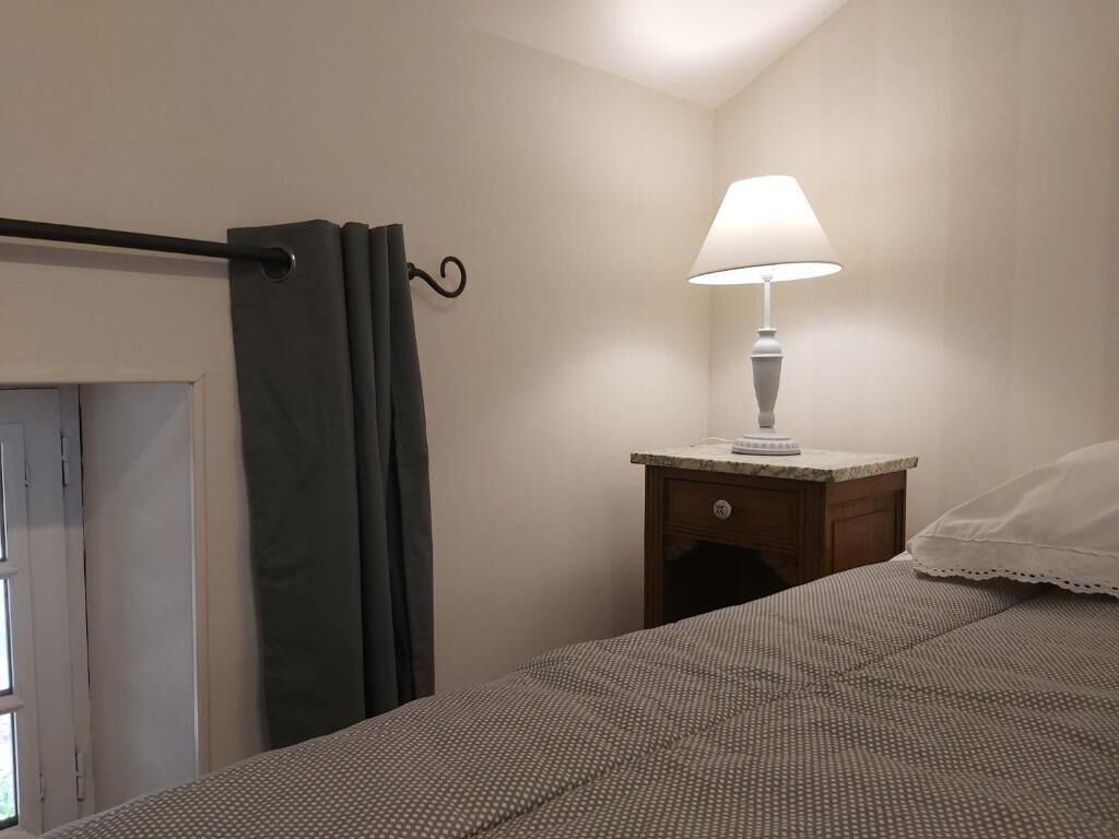 A bedroom with a bed, a nightstand with a lamp, a curtain, and a door.
